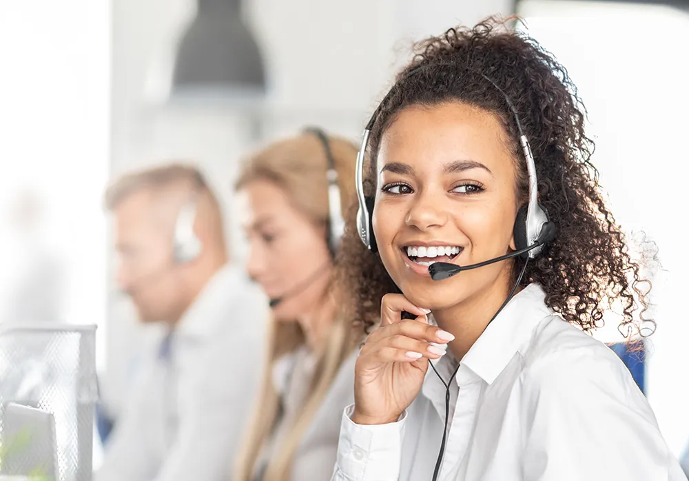 Smiling support agent wearing a headset, with colleagues behind her