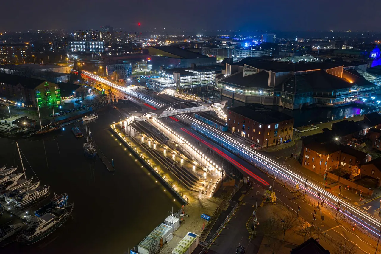 Aerial view at night of a lit dual carriageway, footbridge and marina